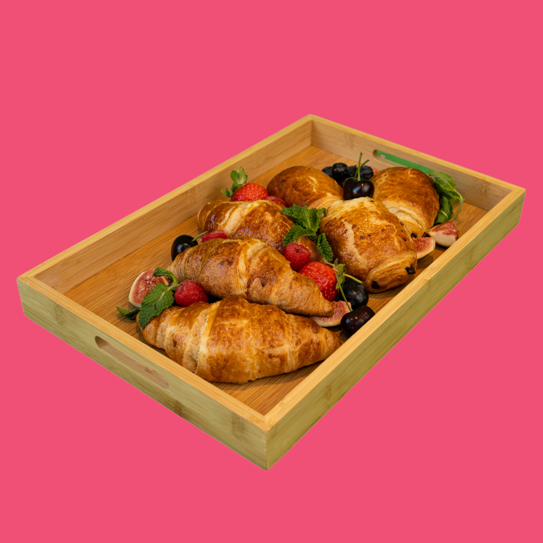 Wooden tray with croissants, berries, and figs on a pink background