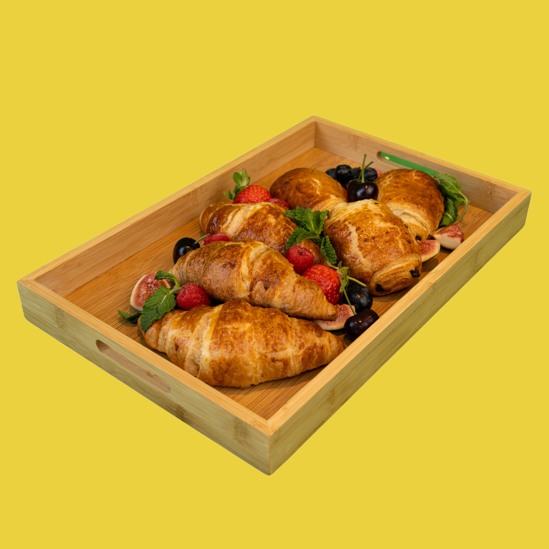 Wooden tray with croissants, berries, and figs on a yellow background